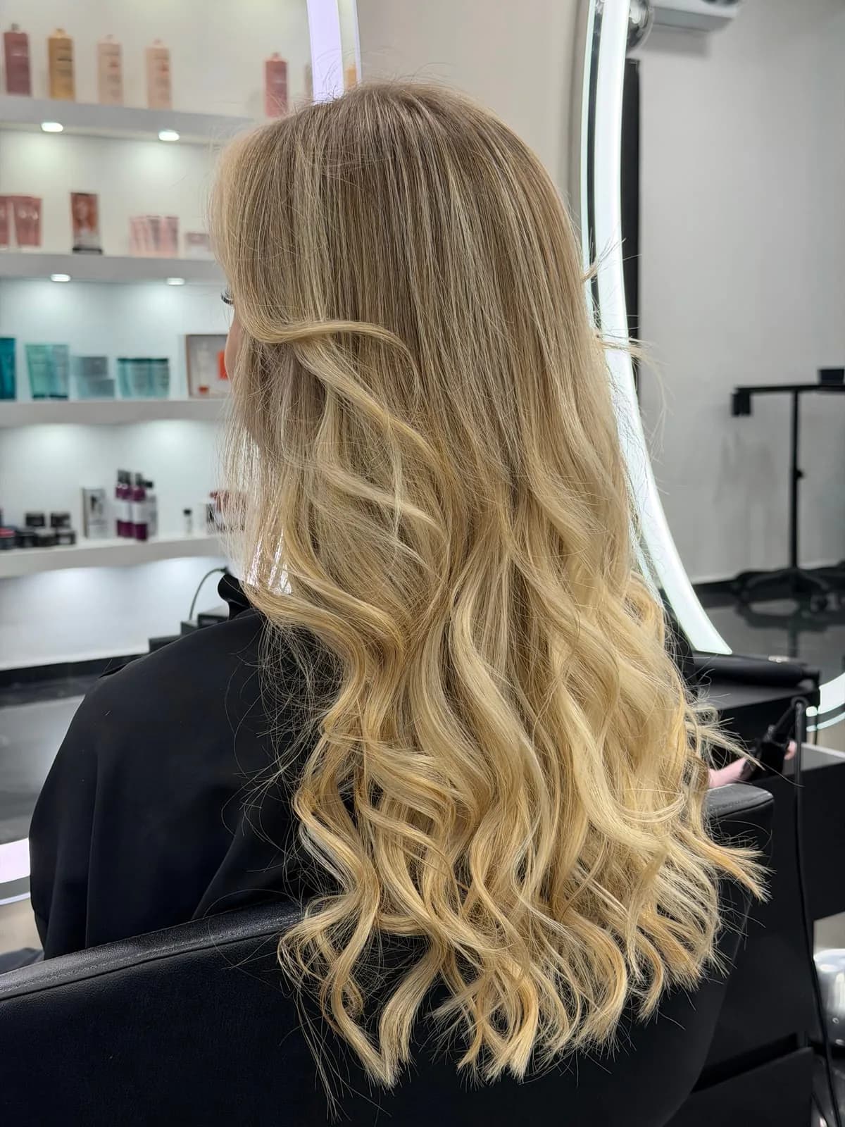 Longue chevelure blonde bouclée éclaircie en balayage, réalisée par un coloriste Jean Bonan