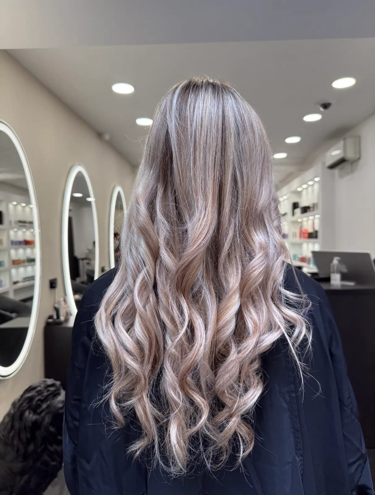 Longs cheveux bouclés éclaircis en balayage blond cendré fondu, réalisé au salon Jean Bonan