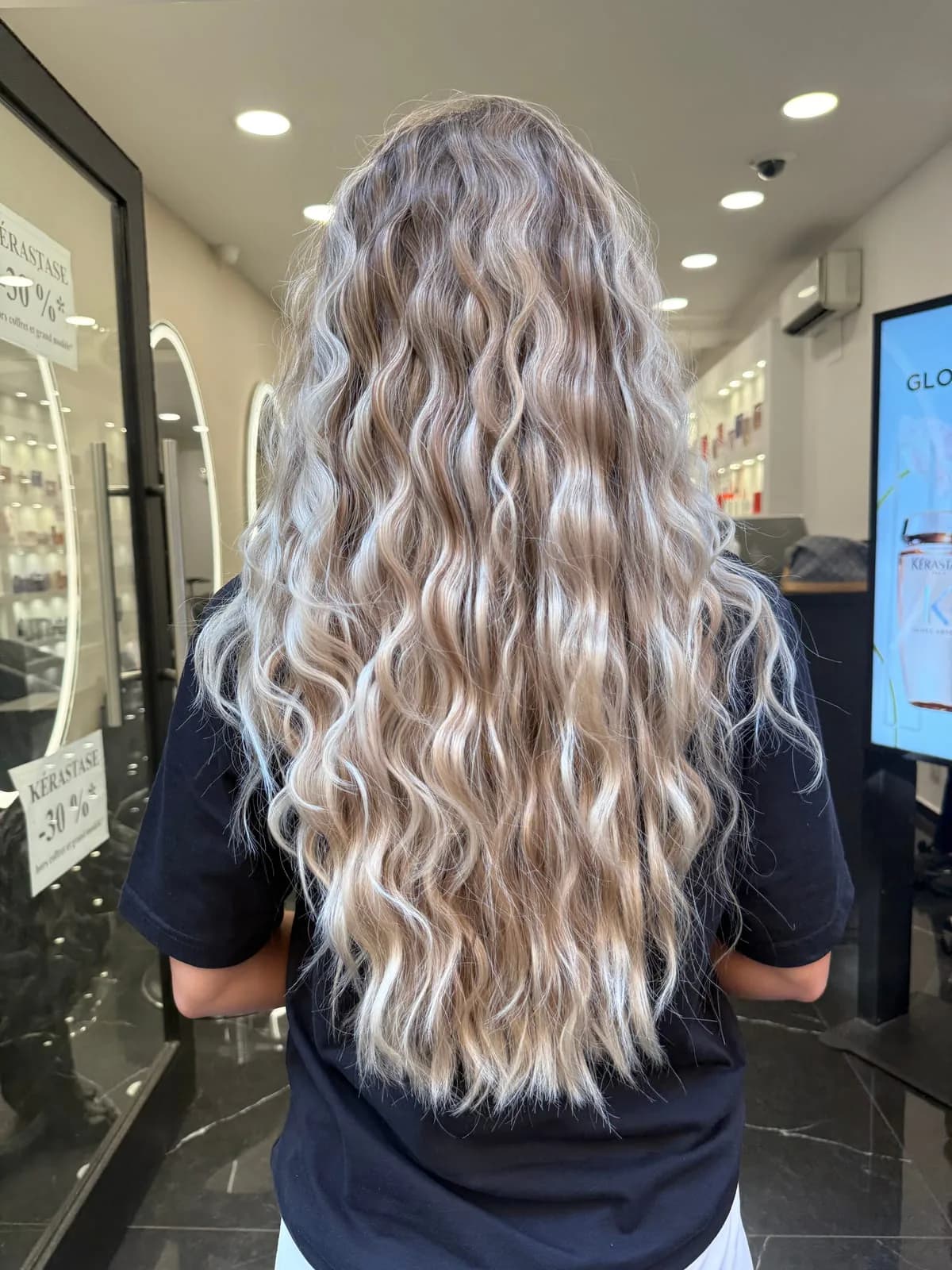 Longs cheveux bouclés blond cendré avec balayage, entretenus dans un salon Jean Bonan